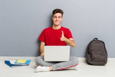 Evinin zemininde dizüstü bilgisayar tutan genç bir öğrenci.