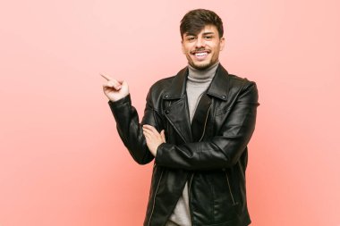 Deri ceketli genç İspanyol adam işaret parmağıyla işaret ederek gülümsüyor..