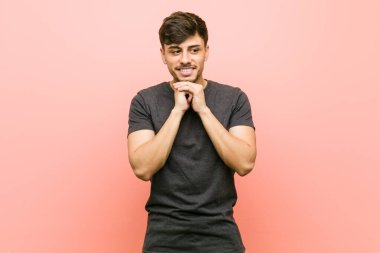 Genç Latin asıllı sıradan bir adam ellerini çenesinin altında tutuyor ve mutlu bir şekilde yan tarafa bakıyor..