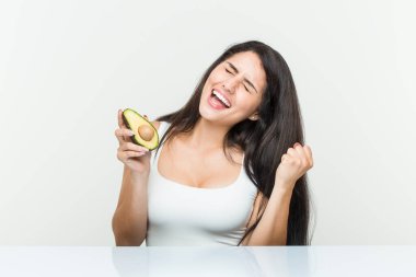 Avokado tutan genç İspanyol kadın tasasız ve heyecanlı bir şekilde tezahürat yapıyor. Zafer konsepti.