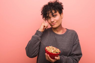 Genç Afrikalı Amerikalı kadın elinde mısır gevreği kasesiyle şakağını işaret ediyor, düşünüyor ve bir göreve odaklanıyor..