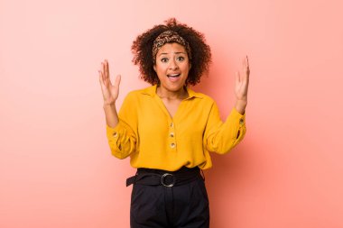 Genç Afrikalı Amerikalı kadın pembe bir arka plana karşı hoş bir sürpriz alıyor, heyecanlı ve el kaldırıyor..