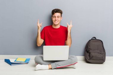 Evinin zemininde dizüstü bilgisayar tutan genç bir öğrenci.