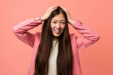 Pembe takım elbiseli genç Çinli kadın ellerini başının üstünde tutarak neşe içinde gülüyor. Mutluluk kavramı.