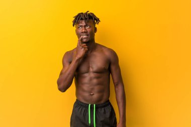Genç siyah adam gömleksiz mayo giyen şüpheli ve şüpheci ifade ile yan bakıyor.