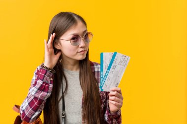 Genç Asyalı kadın elinde uçak biletleriyle bir dedikoduyu dinlemeye çalışıyor..