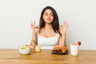 Genç kıvrımlı kadın kahvaltı yapıyor. Sıkı çalışma gününden sonra rahatlıyor. Yoga yapıyor..