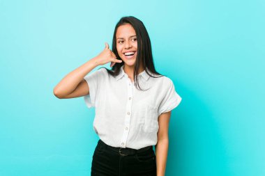 Young hispanic cool woman against a blue wall showing a mobile phone call gesture with fingers.