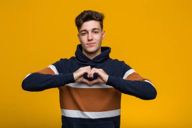 Young cool man wearing a hoodie smiling and showing a heart shape with him hands. clipart