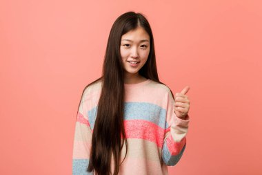 Genç havalı Çinli kadın gülümsüyor ve başparmağını kaldırıyor.