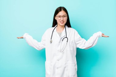 Genç Çinli doktor kadın kollarıyla terazi yapıyor, mutlu ve kendinden emin..