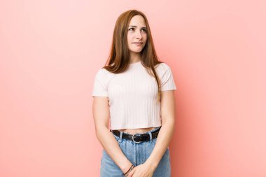 Genç kızıl saçlı kadın pembe duvarın karşısında şaşkın, kuşkulu ve kararsız hissediyor..