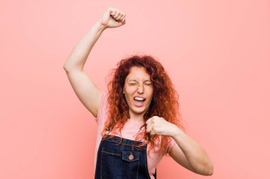 Kot pantolon giyen kızıl saçlı genç bir kadın özel bir günü kutluyor, atlıyor ve enerji dolu kollarını kaldırıyor..