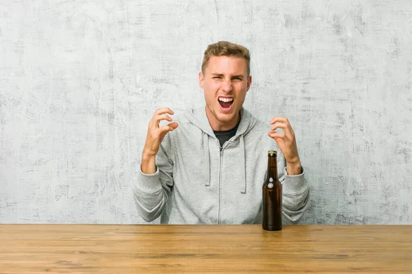 Młody Człowiek Pijący Piwo Stole Zdenerwowany Krzykiem Napiętymi Rękami — Zdjęcie stockowe