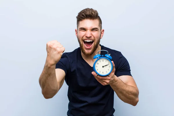 Young Caucasian Man Holding Alarm Clock Cheering Carefree Excited Victory — Stock Photo, Image