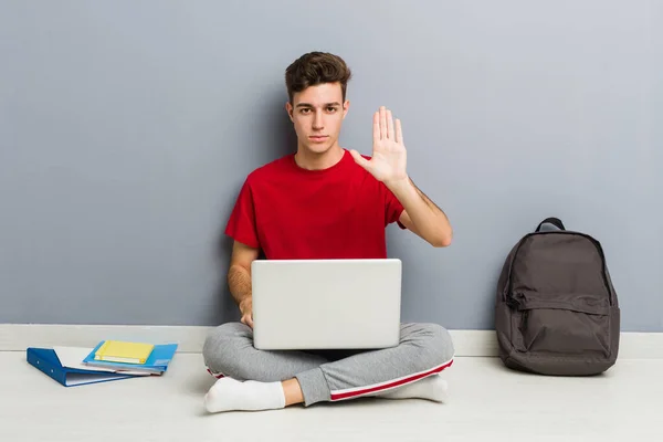 Young student man sitting on his house floor holding a laptop