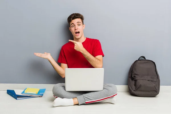 Joven estudiante sentado en el piso de su casa sosteniendo un portátil — Foto de Stock