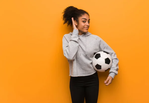 Młoda Czarna Kobieta Fitness Próbuje Słuchać Plotek Trzymanie Piłki Nożnej — Zdjęcie stockowe