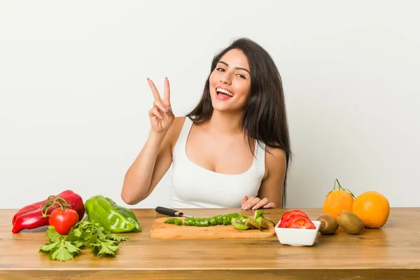 Młoda Zakrzywiona Kobieta Przygotowuje Zdrowy Posiłek Pokazując Znak Zwycięstwa Uśmiechając — Zdjęcie stockowe