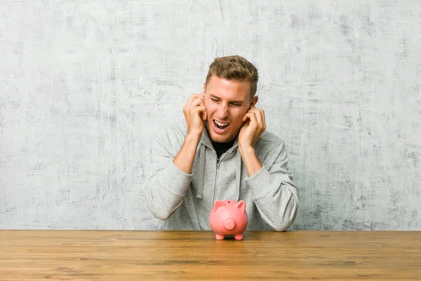 Jeune Homme Économiser Argent Avec Une Tirelire Couvrant Les Oreilles — Photo