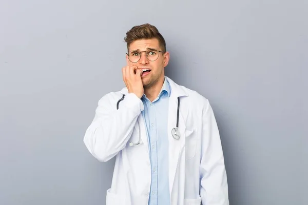 Młody Blondynka Lekarz Człowiek Obgryzanie Paznokcie Nerwowy Bardzo Zaniepokojony — Zdjęcie stockowe