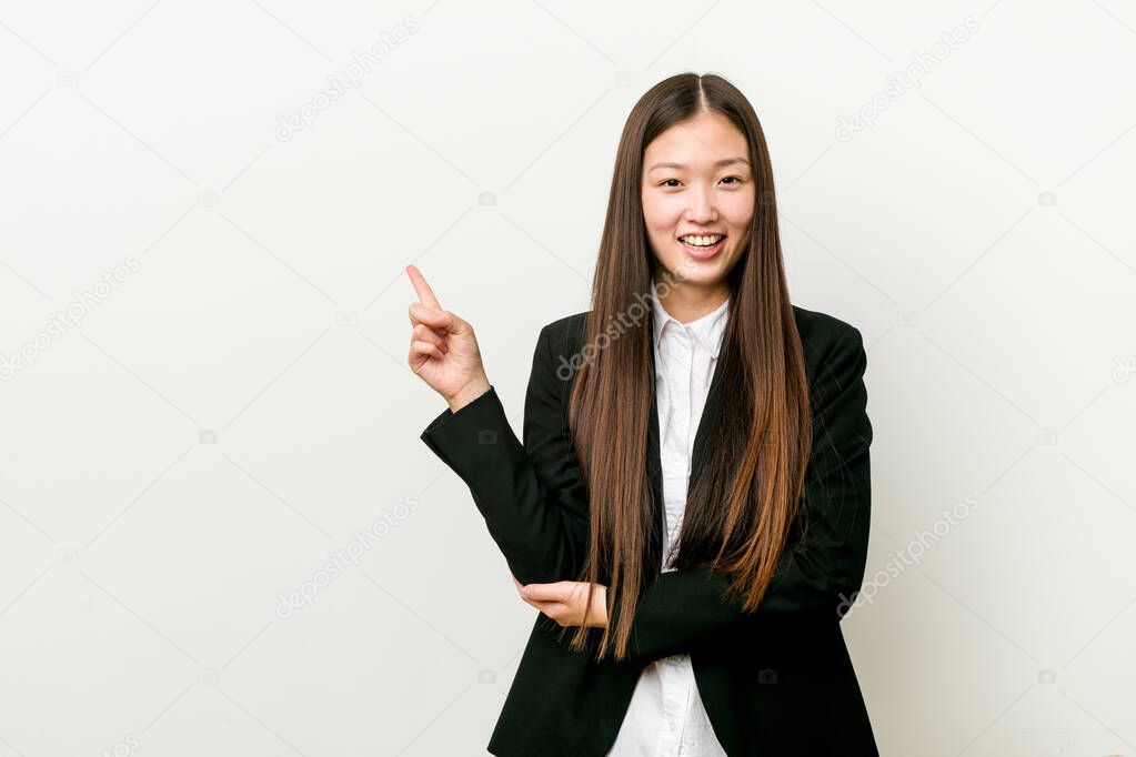 Young pretty chinese business woman smiling cheerfully pointing with forefinger away.