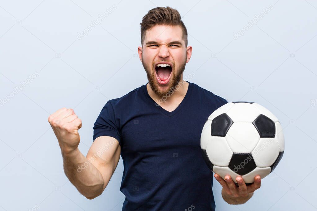 Young caucasian man holding a soccer ball cheering carefree and excited. Victory concept.