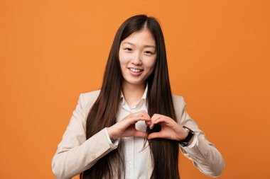 Young business chinese woman smiling and showing a heart shape with him hands.