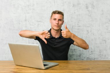 Genç girişimci dizüstü bilgisayarıyla bir masanın üzerinde çalışıyor. Baş parmaklarını yukarı kaldırmıyor, zor bir seçim konsepti.