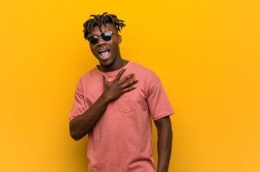 Güneş gözlüğü takan genç siyahi adam elini göğsüne koyup kahkahalar atıyor..