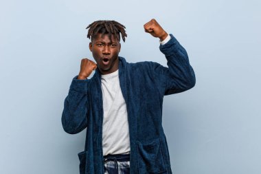 Genç Afrikalı siyah adam pijama giyiyor zafer sonrası yumruğunu kaldırıyor, kazanan konsept.