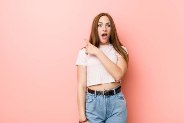 Kızıl saçlı genç bir kadın pembe bir duvara dayanıyor.