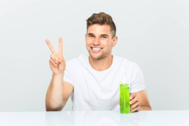 Genç yakışıklı adam aloe vera şişesi tutuyor. İki numarayı parmaklarıyla gösteriyor..