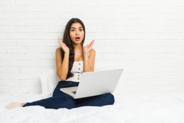 Young arab woman working with her laptop on the bed surprised and shocked.