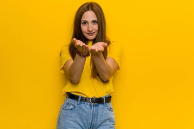 Kızıl saçlı genç kadın elinde avuç içi bir şeyle kameraya sunuyor..