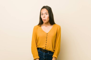 Young hispanic woman against a beige background shrugs shoulders and open eyes confused. clipart