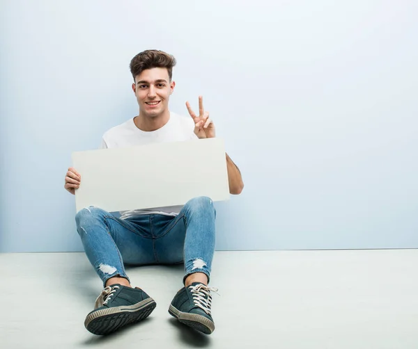 Joven Sosteniendo Cartel Sentado Piso Casa Mostrando Número Dos Con — Foto de Stock