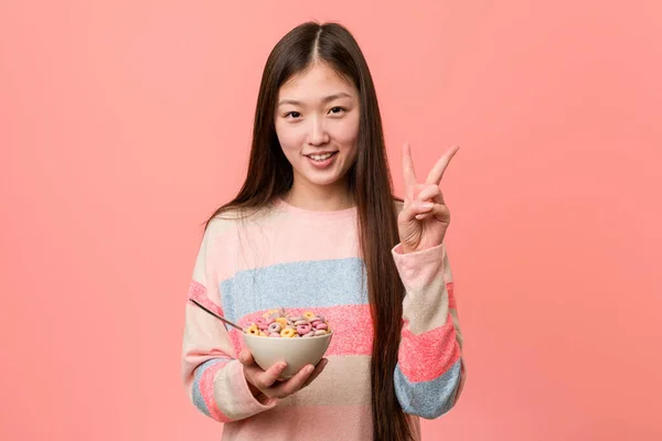 年轻的亚洲女人 手里拿着一个麦片碗 手里拿着两个手指 — 图库照片