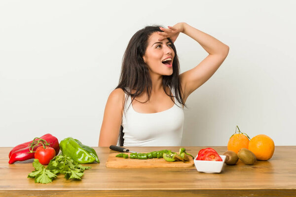 Молодая пышная женщина готовит здоровую пищу глядя далеко держа руку на лбу
.