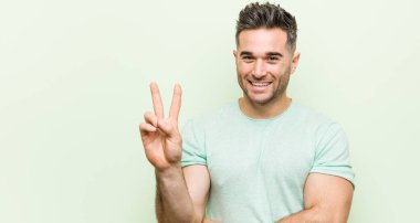 Yeşil arka planda genç ve yakışıklı bir adam iki numarayı parmaklarıyla gösteriyor..