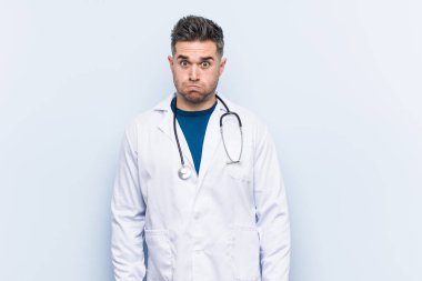 Genç yakışıklı doktor yanakları üflüyor, yorgun bir ifadesi var. Yüz ifadesi kavramı.