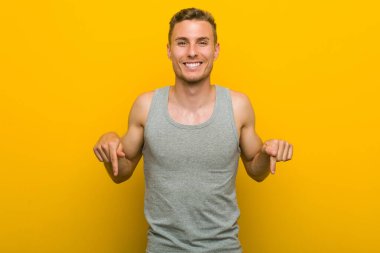 Beyaz tenli genç sporcu parmaklarıyla aşağıyı işaret ediyor, pozitif duygu..