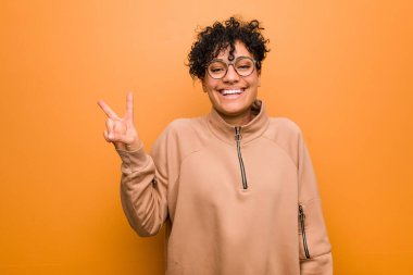Young mixed african american woman against a brown background showing victory sign and smiling broadly.