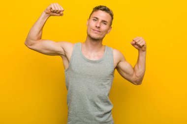 Beyaz tenli genç adam güçlü bir jest yapıyor, kollarıyla, kadınsı gücün sembolü.