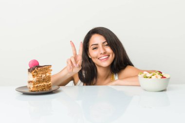 Genç İspanyol kadın iki numarayı parmaklarıyla gösteren pasta ve meyve arasında seçim yapıyor..