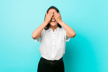 Mavi bir duvara yaslanmış genç, Latin asıllı, havalı bir kadın. Elleriyle gözlerini kapatıyor. Gülümsüyor ve bir sürpriz bekliyor..