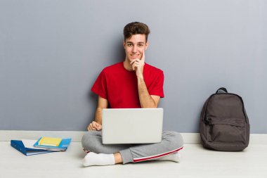 Evinin zemininde dizüstü bilgisayar tutan genç bir öğrenci.