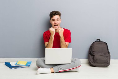 Evinin zemininde dizüstü bilgisayar tutan genç bir öğrenci.