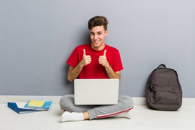 Evinin zemininde dizüstü bilgisayar tutan genç bir öğrenci.