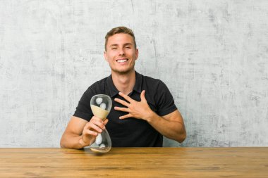 Masada kum saati tutan genç adam elini göğsünde tutarak kahkahalar atıyor..